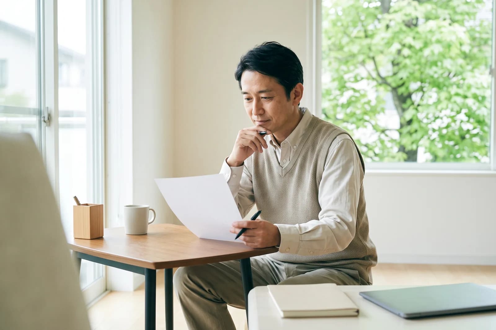 宅建の受験生が、自宅の机で1枚の紙とペンを持ち、開業の費用について考えている様子