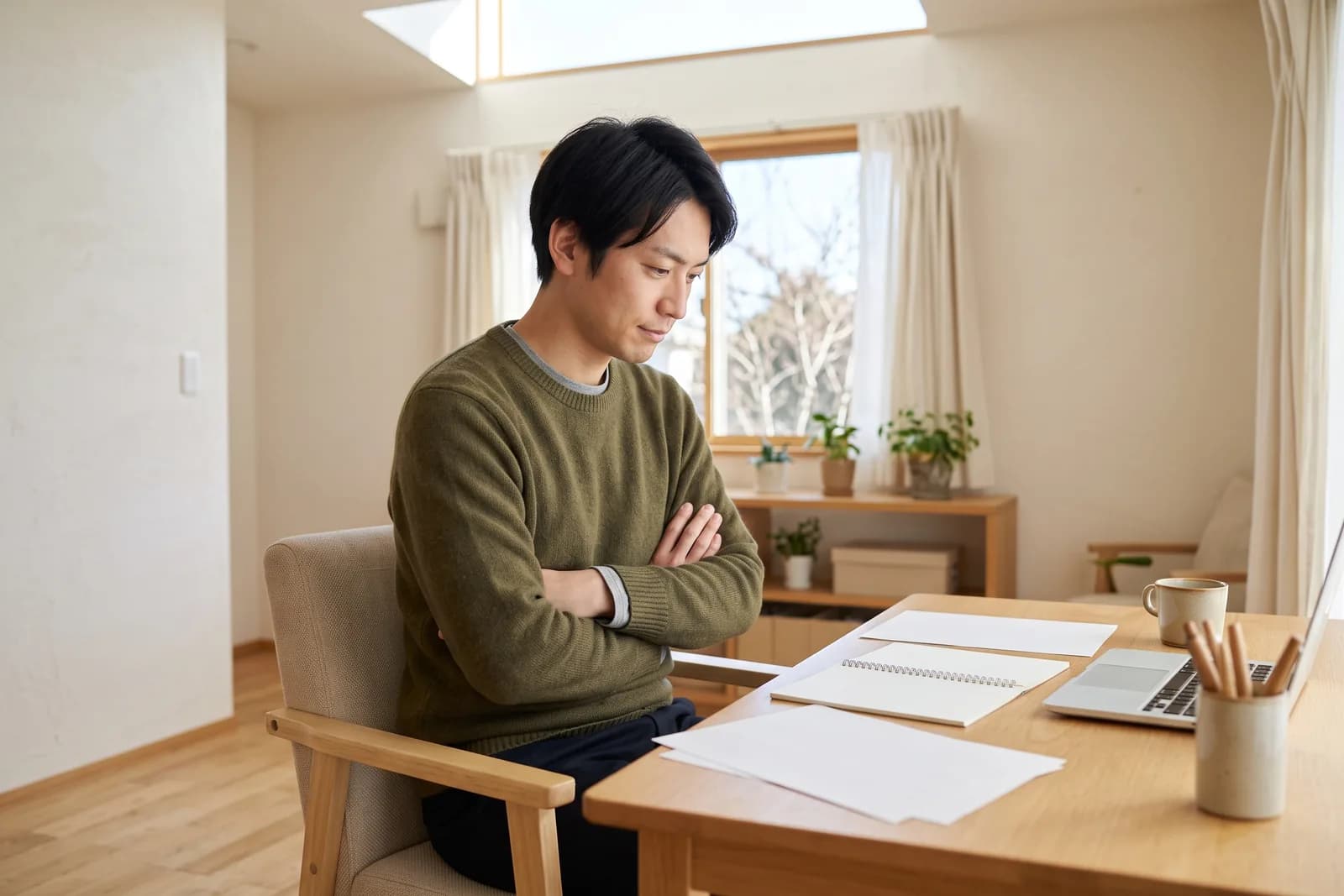 宅建の受験生が、自室の机に向かって腕組みをしながら勉強の計画を立てている様子