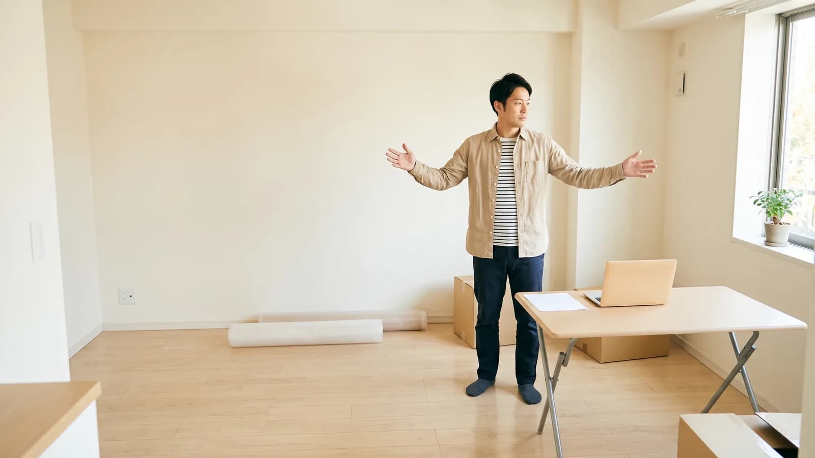 開業準備中の事務所の室内で、開業を考える会社員大家が家具の配置を考えるために両手を広げている様子